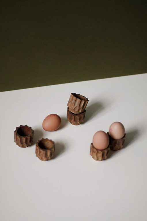 Six unique wooden egg cups, some shown stacked, some shown displaying hard boiled eggs.